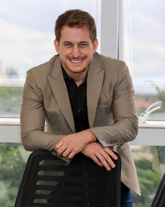 Luciano Serra leaning on a chair by an office window